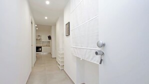 A narrow hallway with white walls and a tiled floor leading to a kitchen area. - YCH Bagnera Suites  (Rome)