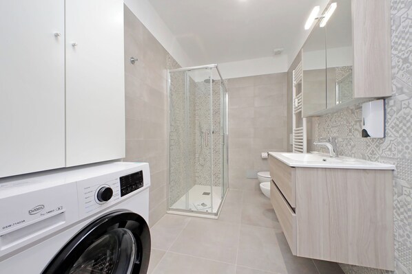 Een moderne badkamer met een douchecabine van glas, een ingebouwde wasmachine en een wastafel met spiegel.