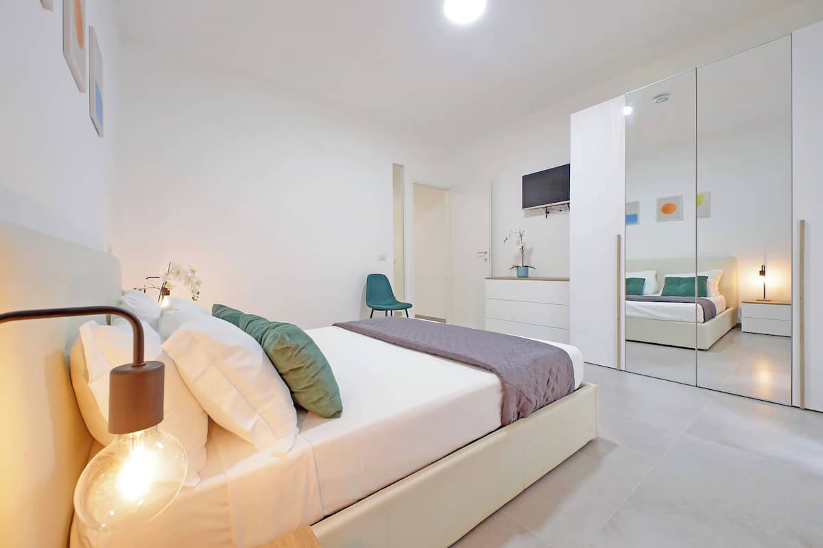 A modern bedroom with a bed, bedside table, and a mirror.