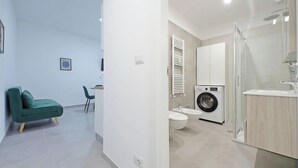 A modern apartment with a living area, a compact bathroom with a washing machine, and a glass shower enclosure. - YCH Bagnera Suites  (Rome)