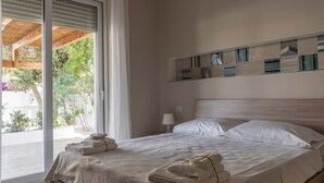 Een net opgemaakt bed met gevouwen handdoeken, een bedlamp en uitzicht op groen door een schuifdeur.