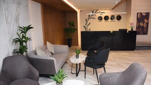 A modern reception area with a sofa, chairs, a reception desk, and potted plants. - Sukoon Hotel Amman (Amman)