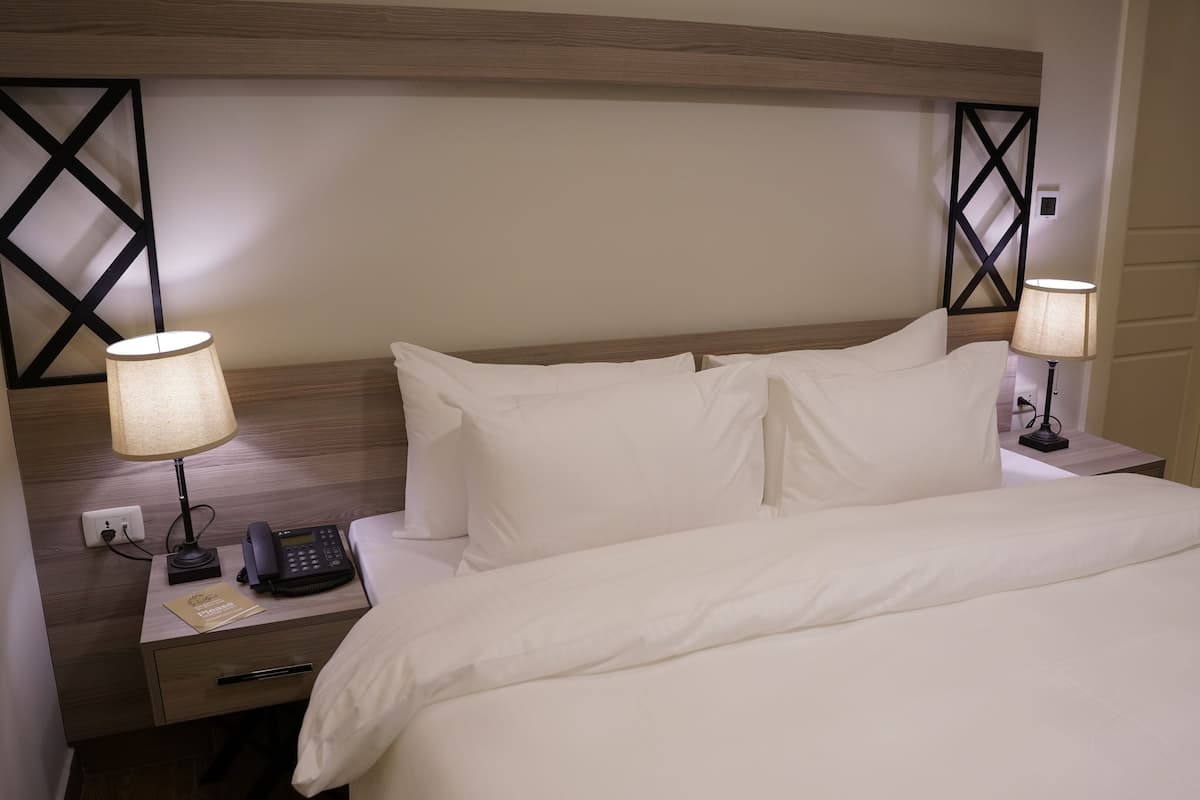 A hotel room with a bed, two bedside tables, a phone, and a lamp on each table.