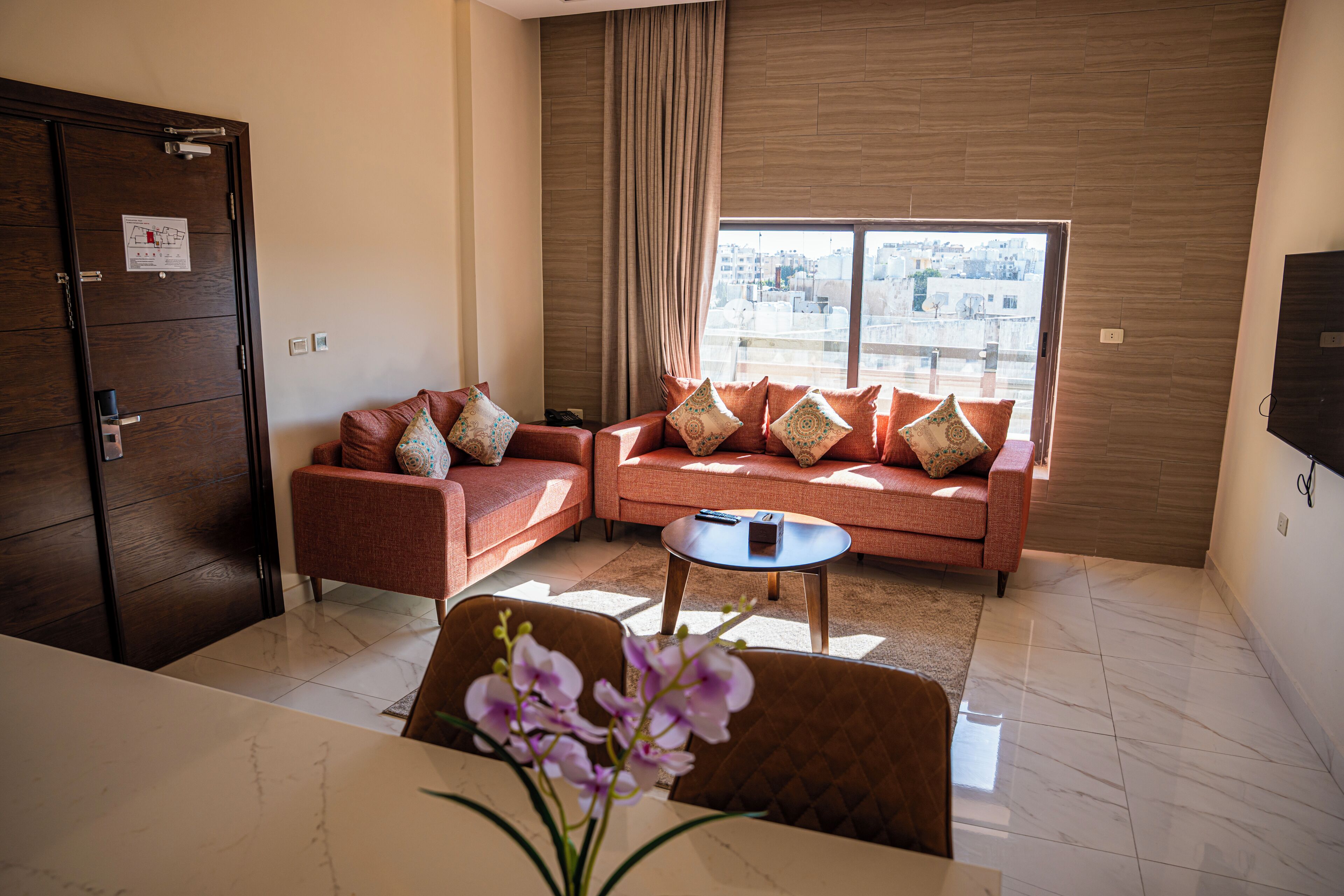 A modern living room with a sofa set, a coffee table, and a view of the city through large windows.