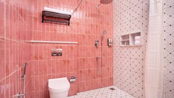 Baño con pared de azulejos rosa, inodoro blanco, zona de ducha y estante con toallas.