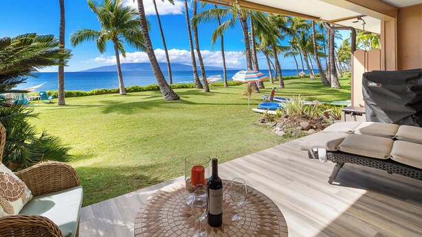 A patio with a view of the ocean, a table with a bottle of wine, and lounge chairs.