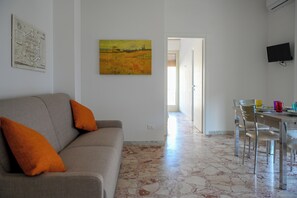 A living room with a sofa, a painting, and a dining area with chairs and a table.