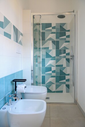 A bathroom with a glass shower enclosure, a bidet, and a toilet.