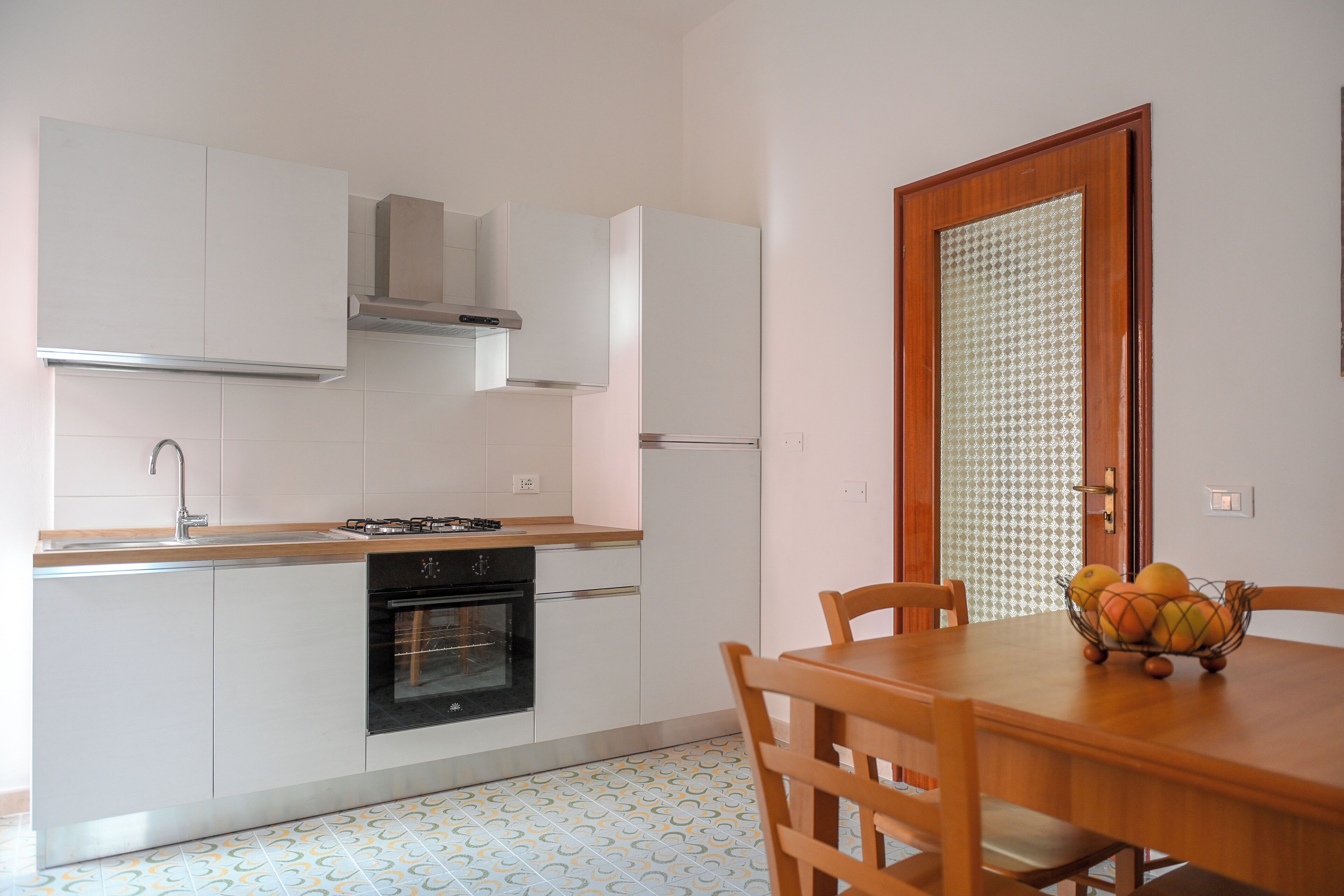 Una cocina con armarios blancos, estufa, horno y una mesa de comedor con sillas.