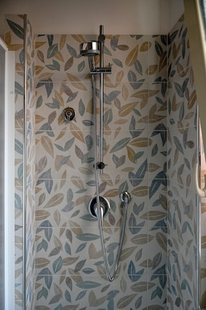 A shower with a leaf-patterned tile wall and a chrome showerhead.