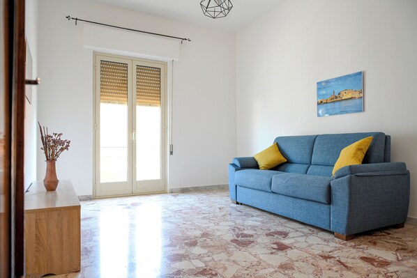 A living room with a blue sofa, wooden floor, and a door with blinds.