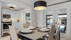 A modern kitchen with white cabinetry, a dining table set for four, and a large window offering a view of the outdoors.