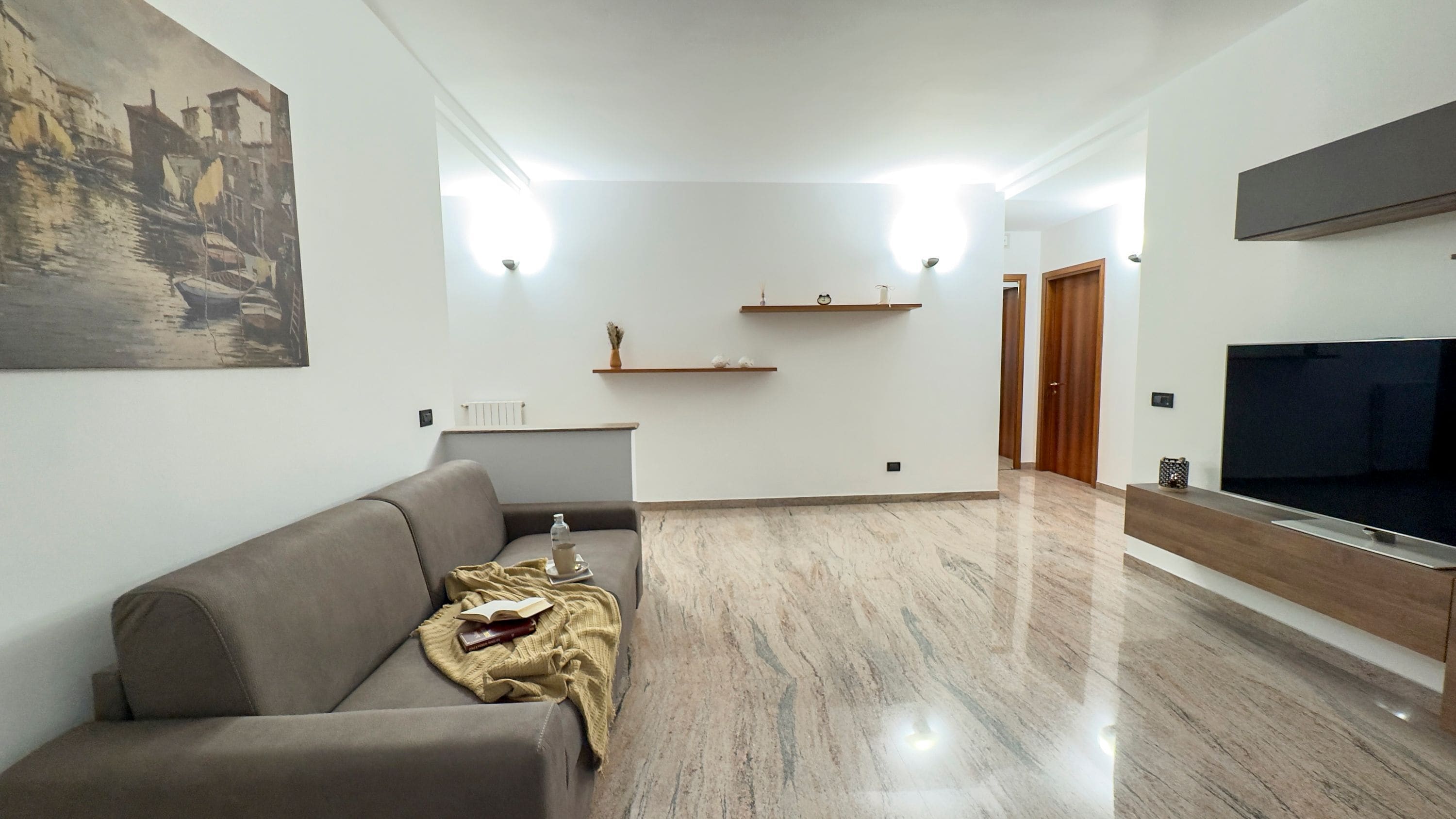 Un salon moderne avec un canapé gris, un téléviseur à écran plat, des étagères en bois et un sol en marbre.