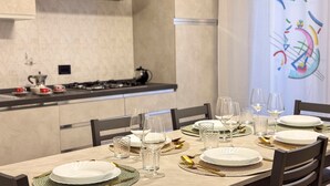 A dining table set with plates, glasses, and cutlery, with a kitchen in the background. - Casa Micio - MS 3 NT by Ca-sa Check (Chioggia)