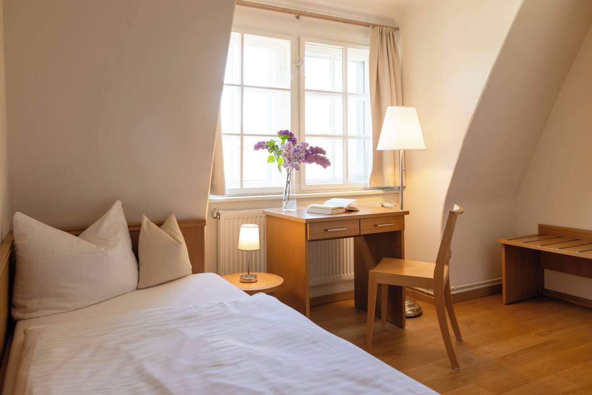 Une chambre d’hôtel équipée d’un lit, d’un bureau, d’une chaise, d’une lampe et d’une fenêtre avec des rideaux.