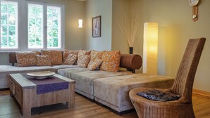 A living room with a sectional sofa, a wooden coffee table, a wicker chair, and a tall floor lamp. - Klosterhotel Lehnin (Kloster Lehnin)