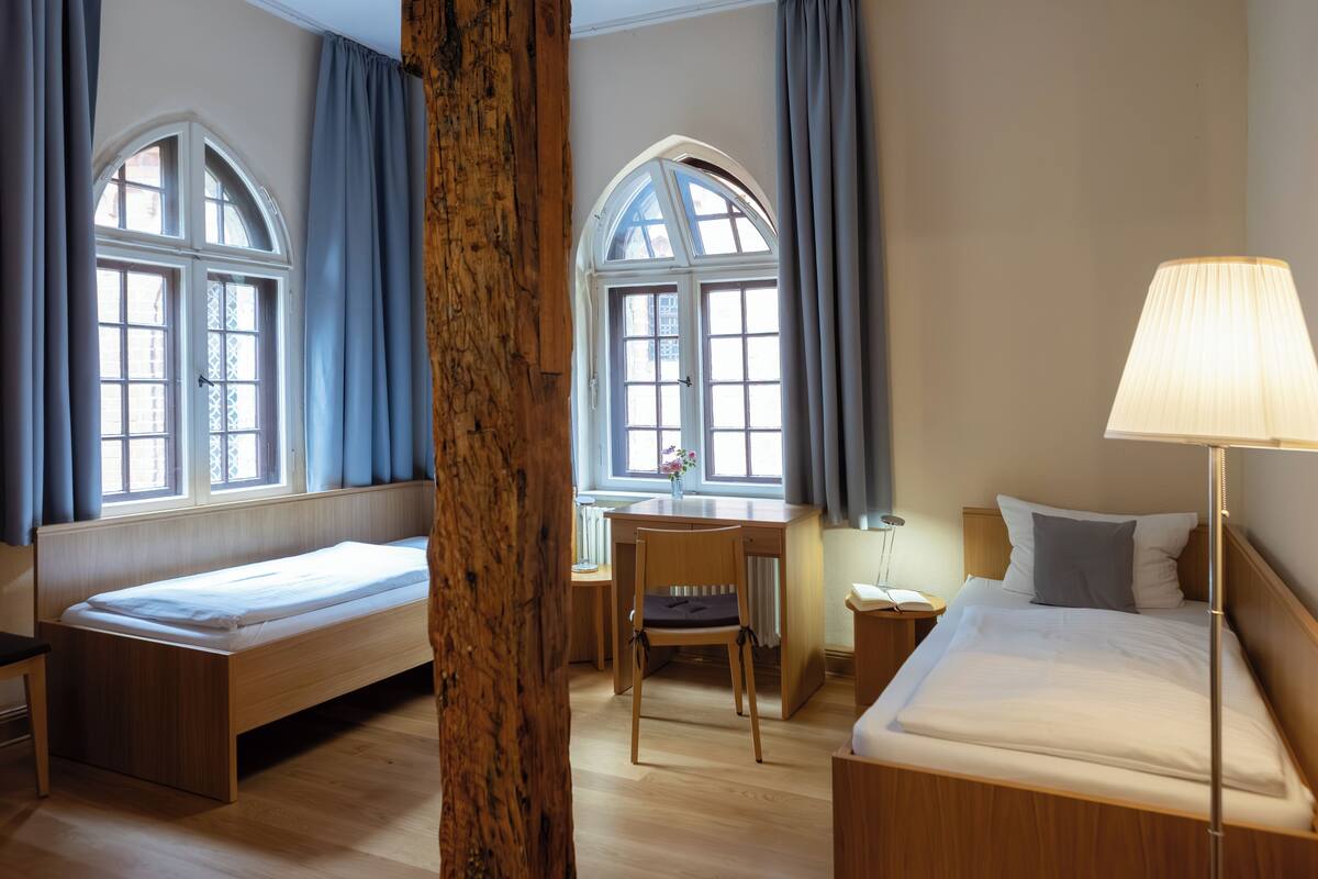 Une chambre d’hôtel avec deux lits simples, un bureau, une chaise et une lampe.