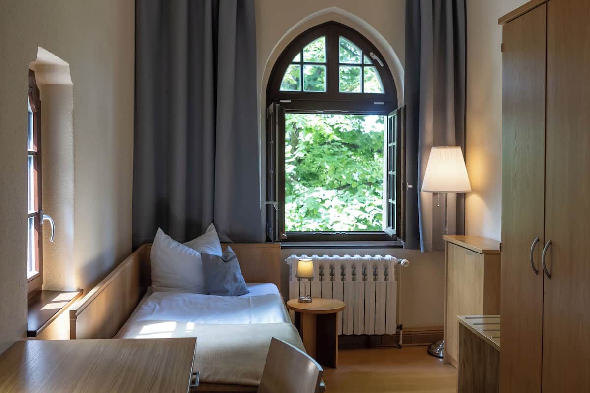 Une chambre à coucher avec un lit, une fenêtre avec des rideaux, une lampe et un radiateur.