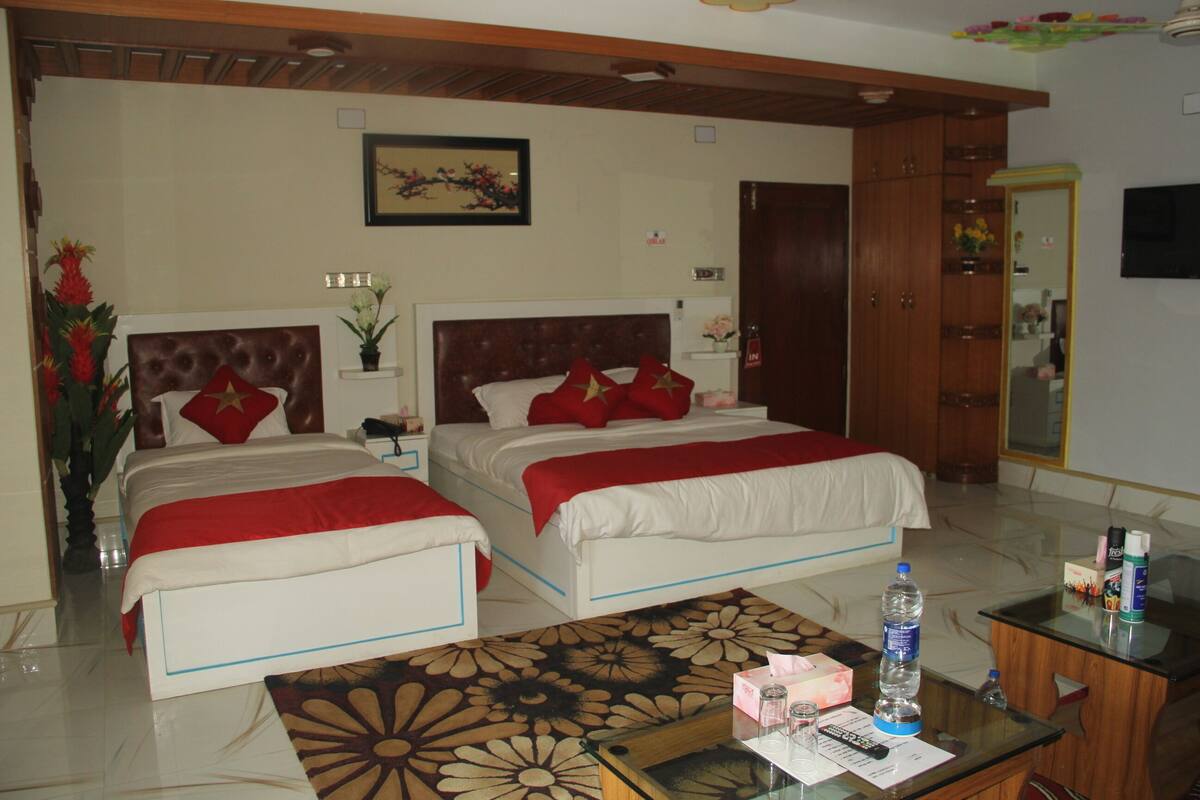 Habitación de hotel con dos camas, techo de madera, decoración floral en la pared, una mesita de noche con una botella de agua, un control remoto y una caja de pañuelos.