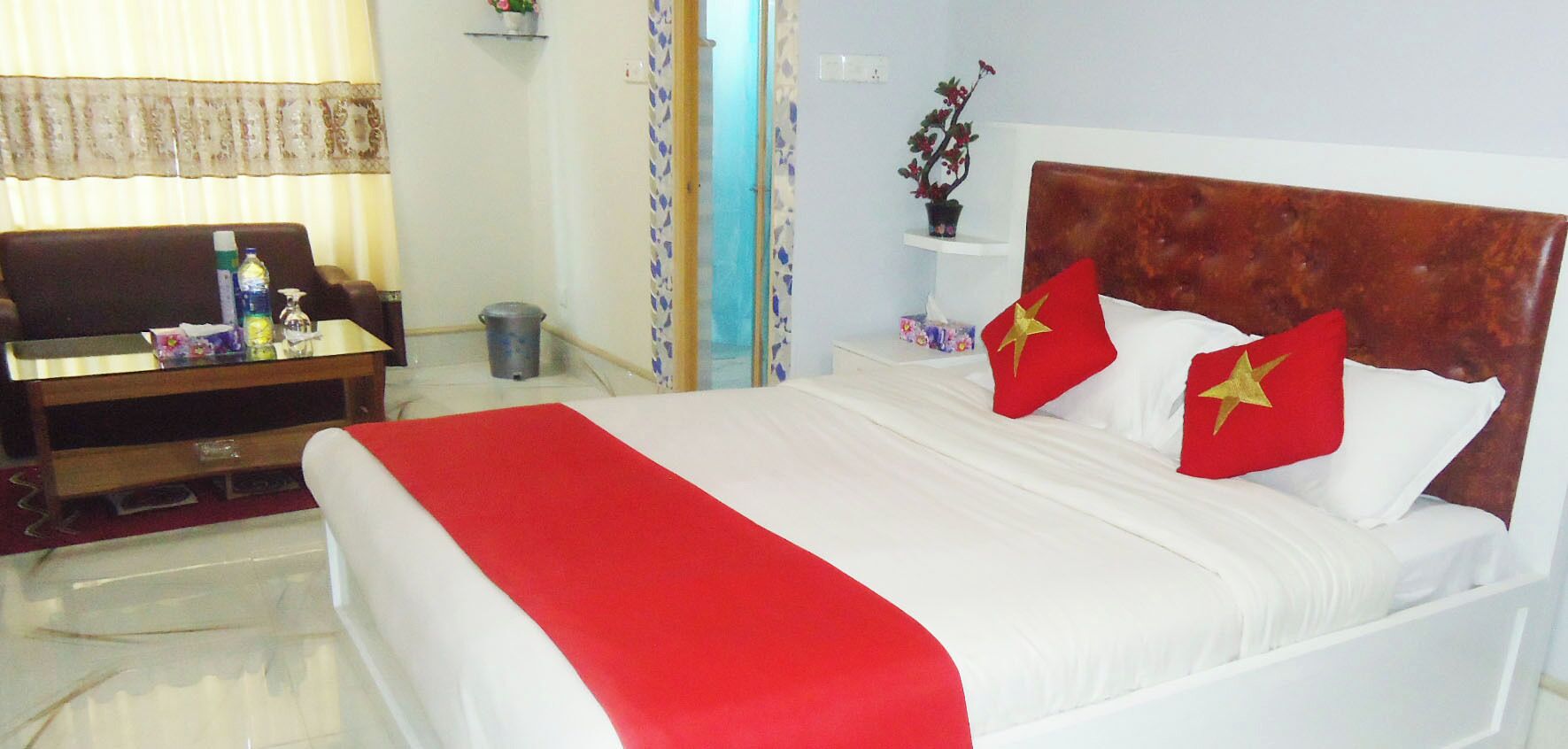Une chambre d’hôtel avec un lit, un bureau, une chaise, une télévision et une petite table sur laquelle se trouvent une bouteille et une boîte de mouchoirs.
