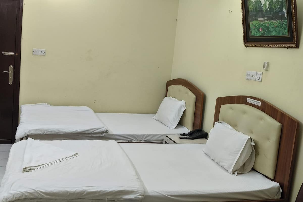 Habitación de hotel con dos camas individuales, una puerta de madera, un escritorio pequeño y un teléfono en la pared.