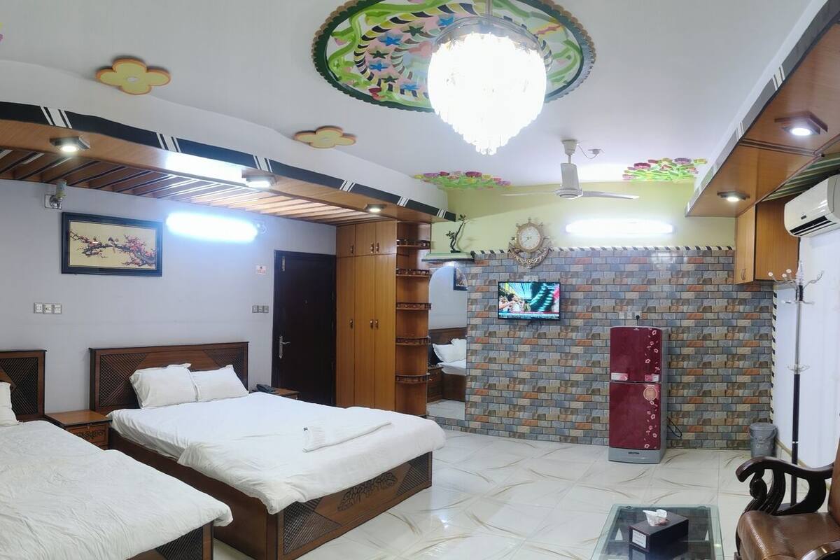 Habitación de hotel con dos camas, televisor, pared de ladrillo, equipo de aire acondicionado y baño con cortina de ducha.