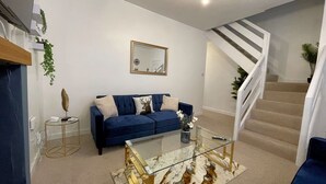 A modern living room with a blue sofa, a glass coffee table, and a staircase. - Beautifully Presented, Cosy Town Centre Cottage - Pass the Keys (Dumfries)