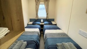 A narrow room with two beds, a window with curtains, a bedside table with a lamp, and a wooden wardrobe. - Cosy 3BR Getaway in Beautiful Country Park - Pass the Keys (Beattock)