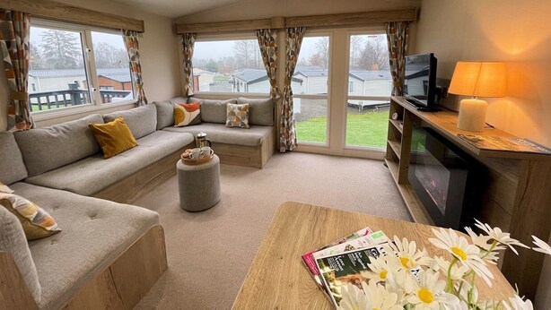 A cozy living room with a sofa, ottoman, and a coffee table with magazines and flowers. - Cosy 3BR Getaway in Beautiful Country Park - Pass the Keys (Beattock)