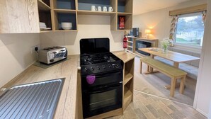 A compact kitchen with a gas stove, a toaster, and wooden shelves above the counter. - Cosy 3BR Getaway in Beautiful Country Park - Pass the Keys (Beattock)