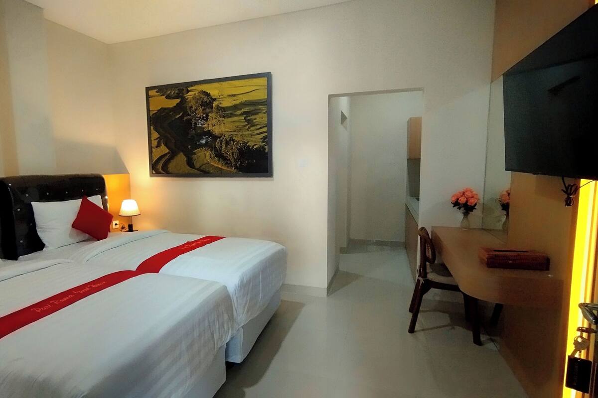 Habitación de hotel con dos camas, un escritorio, una silla, un televisor y un cuadro en la pared.