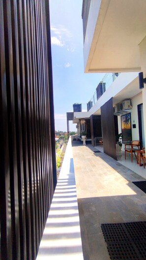 A modern building with a covered outdoor area, a seating area with chairs, and a view of the surrounding landscape. - Puri Rama Guest House Denpasar Bali (Denpasar)