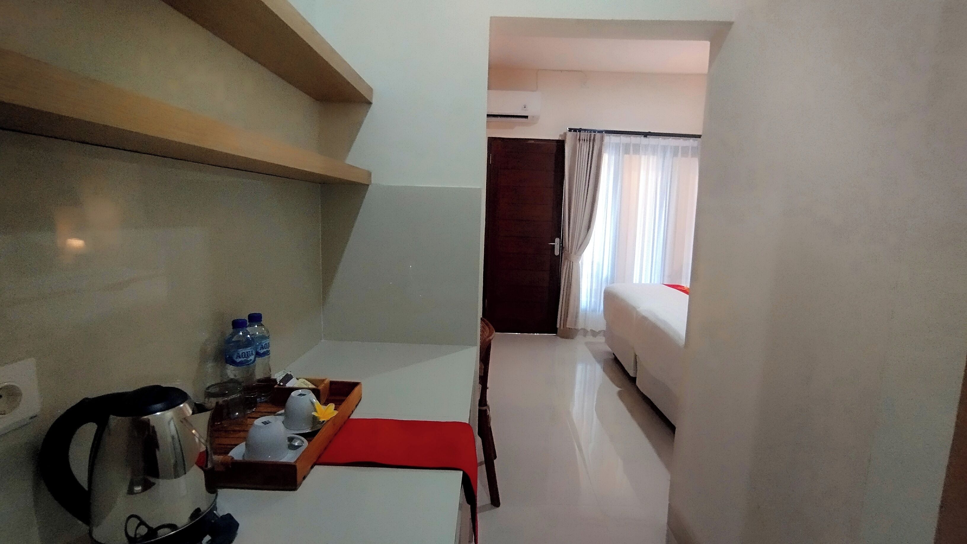 A hotel room with a kitchenette, a bed, a window with curtains, and a small table with a tray of items.