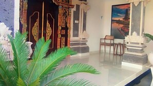 Eine Empfangshalle mit einer großen Kübelpflanze, einer Holztür mit aufwendigen Schnitzereien, einer Steinstatue und einem Gemälde einer Pagode.