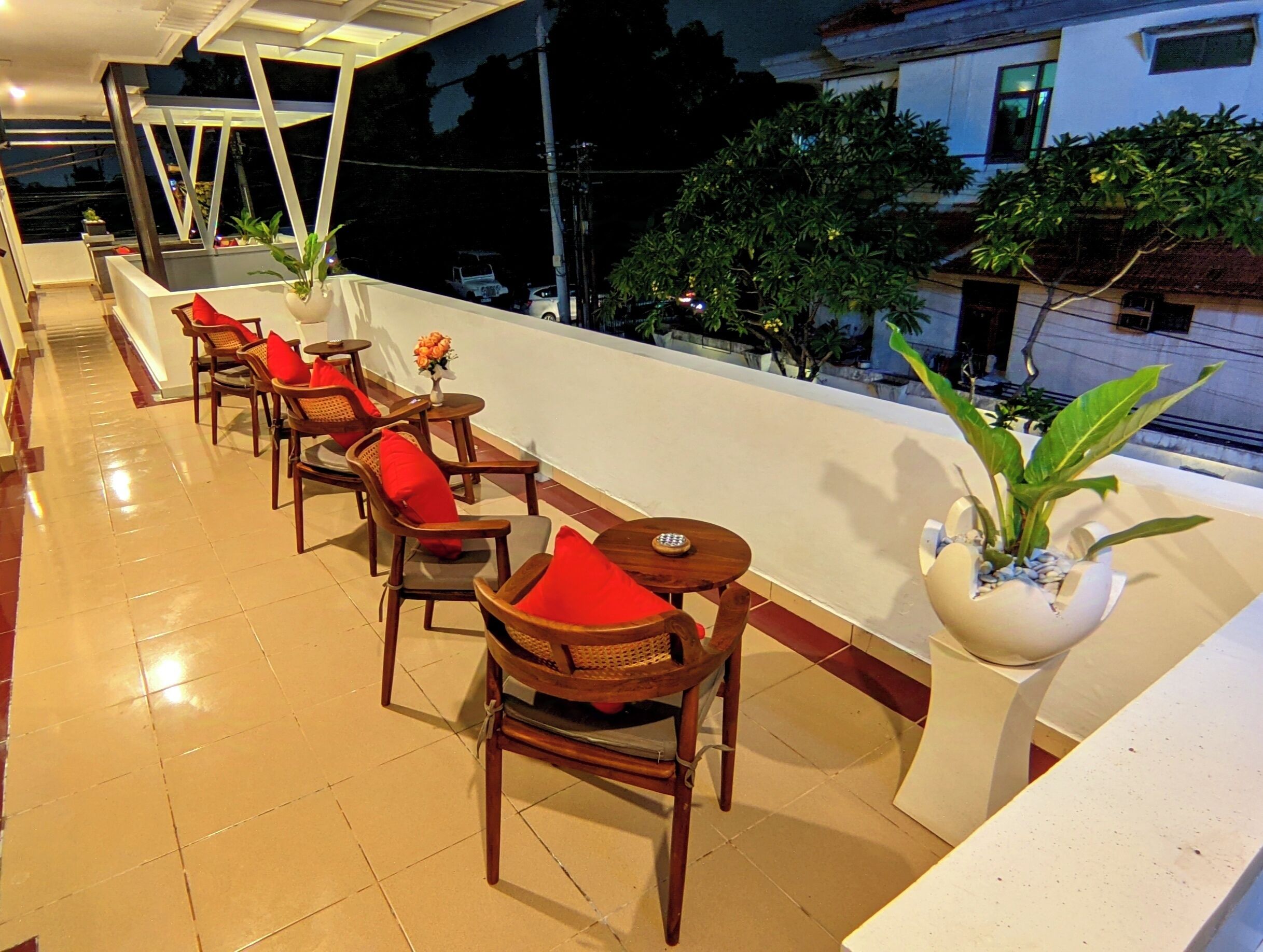 A terrace with wooden chairs and tables, a white railing, and potted plants.