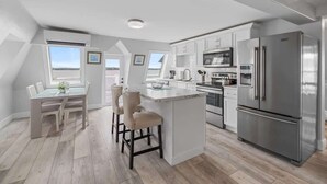 Cocina moderna con una isla central, electrodomésticos de acero inoxidable y un comedor con mesa y sillas.
