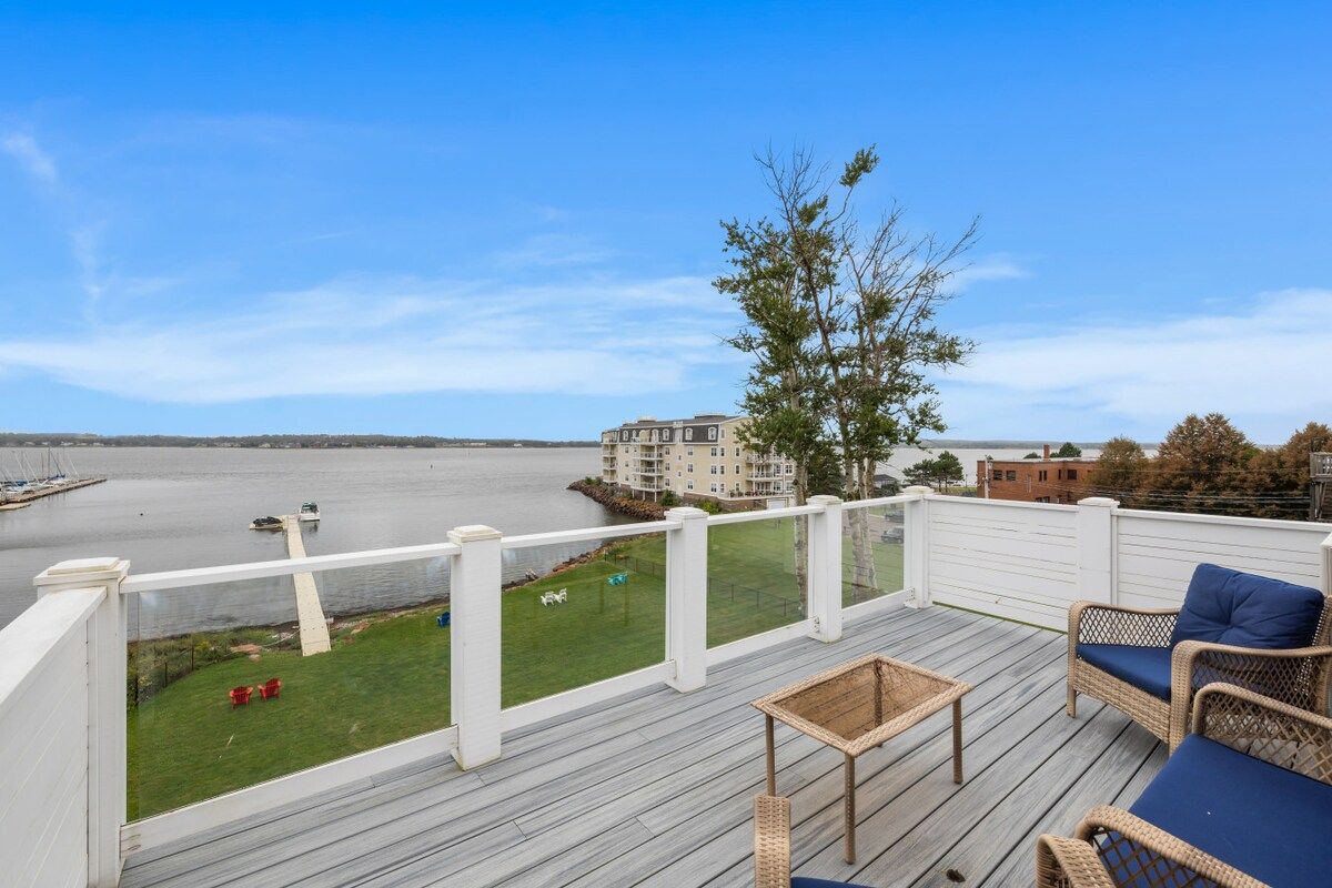 Une terrasse dotée de meubles en osier et offrant une vue sur un plan d’eau.