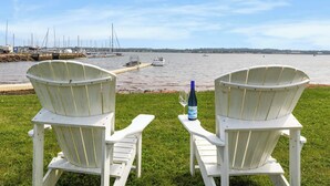 Dos sillas Adirondack blancas mirando hacia un puerto deportivo con barcos y cielo despejado.