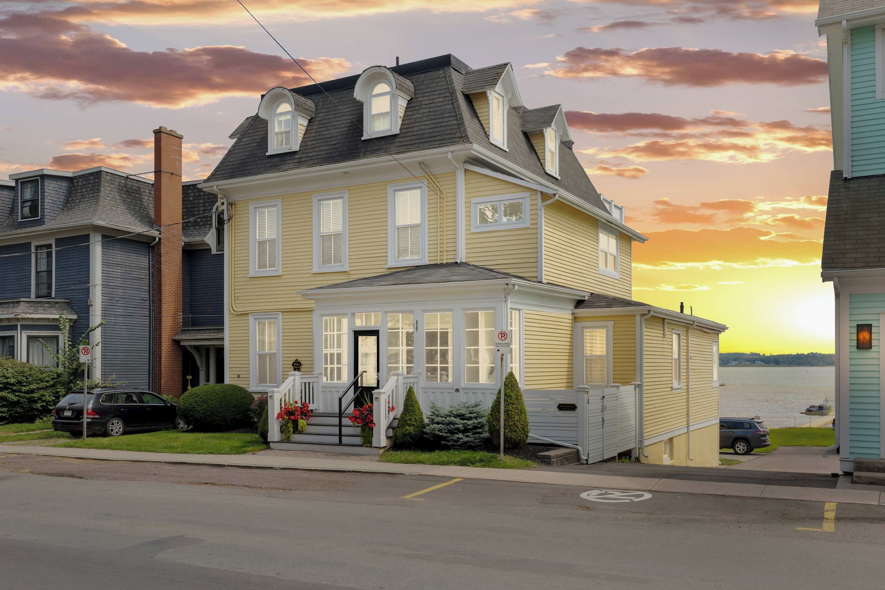 A two-story house with a front porch, a chimney, and a view of a body of water.