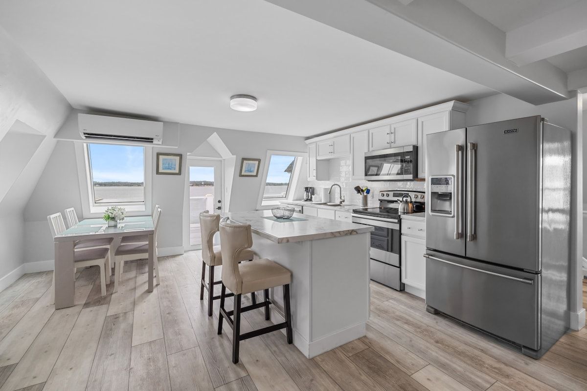A modern kitchen with a central island, stainless steel appliances, and a dining area with a view.