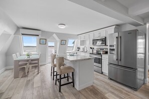 A modern kitchen with a central island, stainless steel appliances, and a dining area with a view. - Waterfront Loft 2 Bedroom Posh Condo Downtown (Charlottetown)