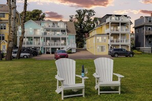 Una hilera de edificios residenciales de varios pisos con balcones, un césped y dos sillas Adirondack blancas con una botella y un vaso.