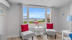Ein modernes Zimmer mit einem großen Fenster, zwei grauen Stühlen, einem kleinen weißen Tisch und einer Lampe.