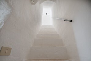 A narrow, white-walled stairway leading to a bright room with a single light fixture on the wall.