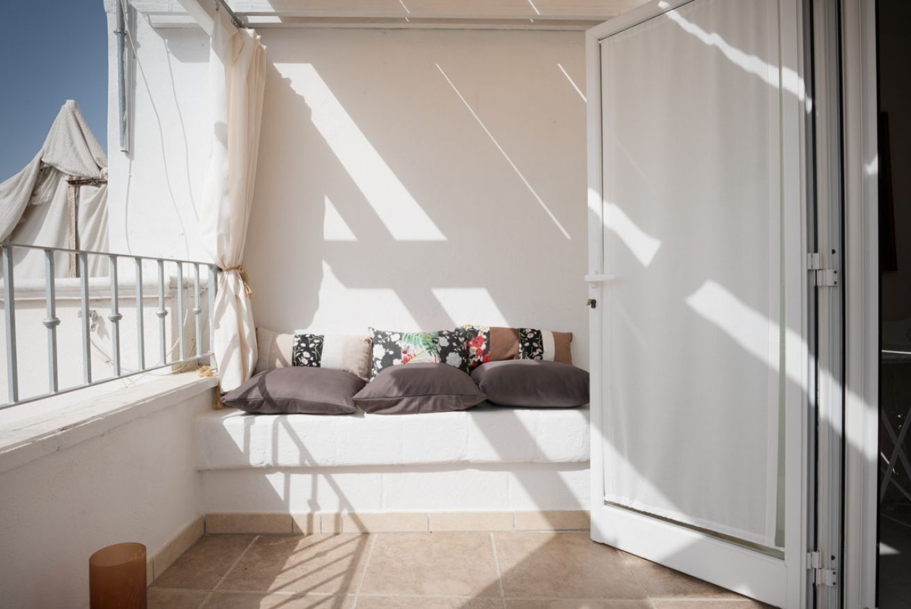 A balcony with a white sofa, beige cushions, and a view of the sky.
