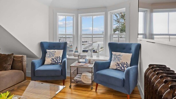 A modern living room with two blue armchairs, a wooden coffee table, and a view of the sea through large windows.