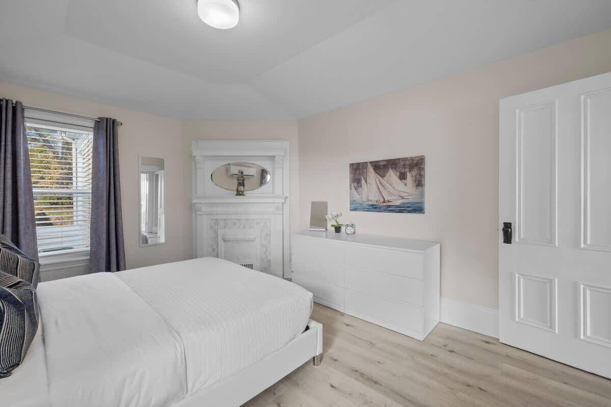 A bedroom with a bed, a dresser, a mirror, a painting, and a door.