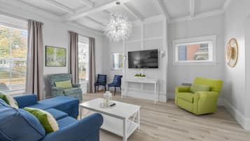 Un salon moderne avec un plafond blanc, un lustre, un téléviseur à écran plat et une grande fenêtre avec des rideaux.