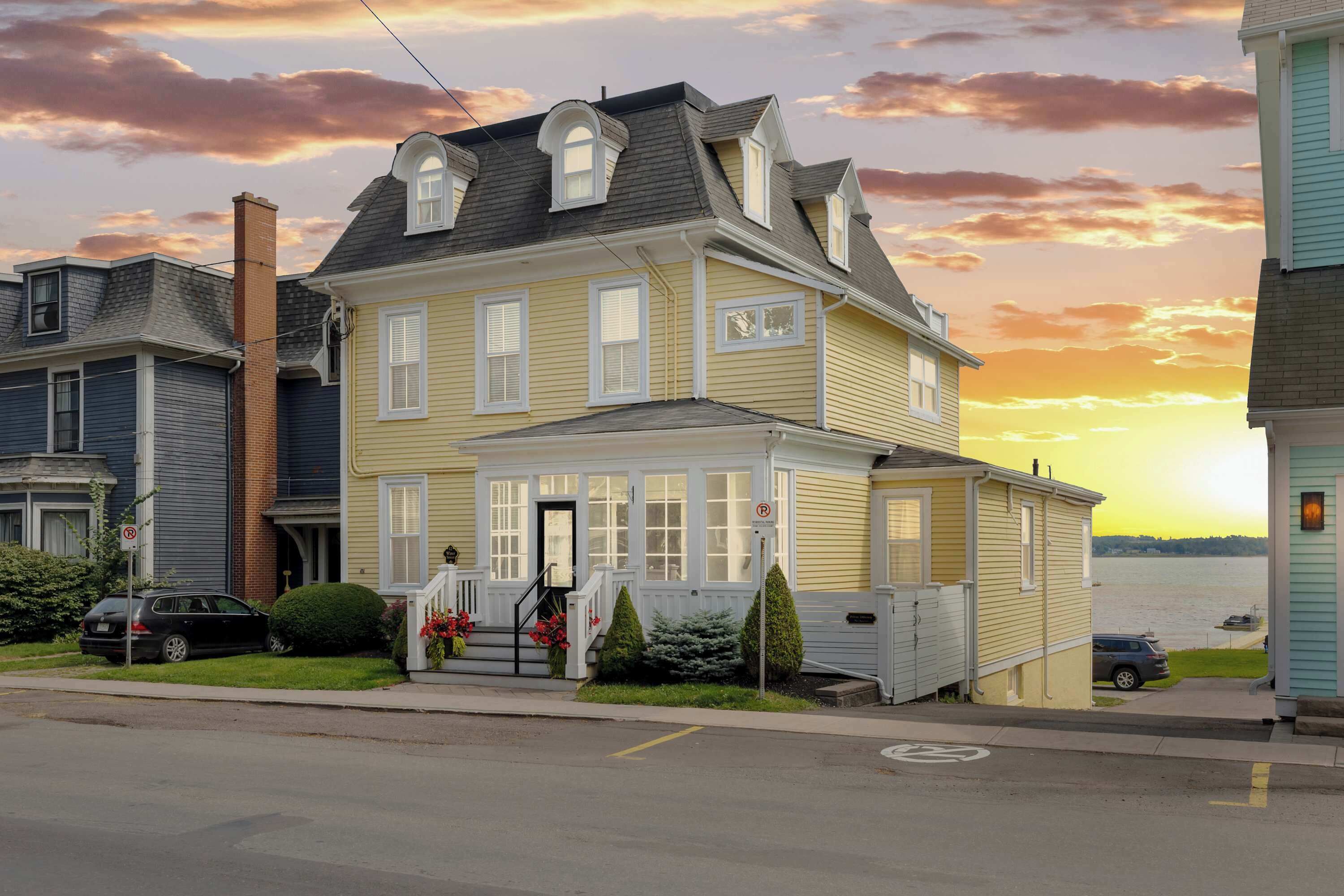 A two-story house with a front porch, a chimney, and a view of a body of water.