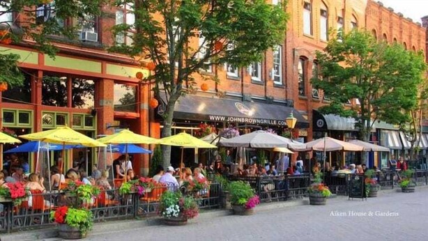 An outdoor seating area with tables and chairs, surrounded by potted plants and umbrellas.